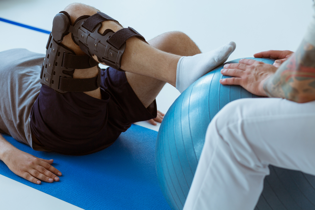 Pretty patient sitting on the blue mat in the gym and training with the ball